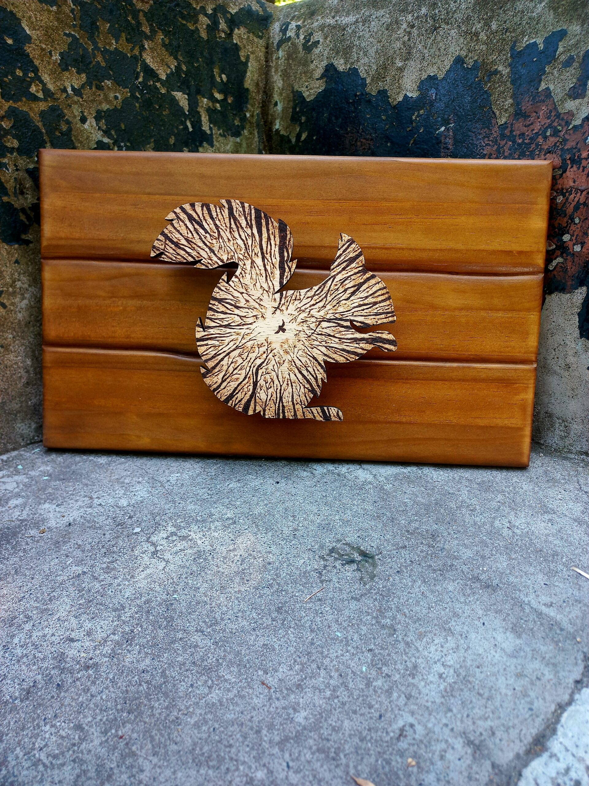 Cadro de madeira composto por unha peza coa silueta dun esquío, cuxo interior mostra un pirogravado que representa a visión do animal desde o chan mirando cara ás copas das árbores.