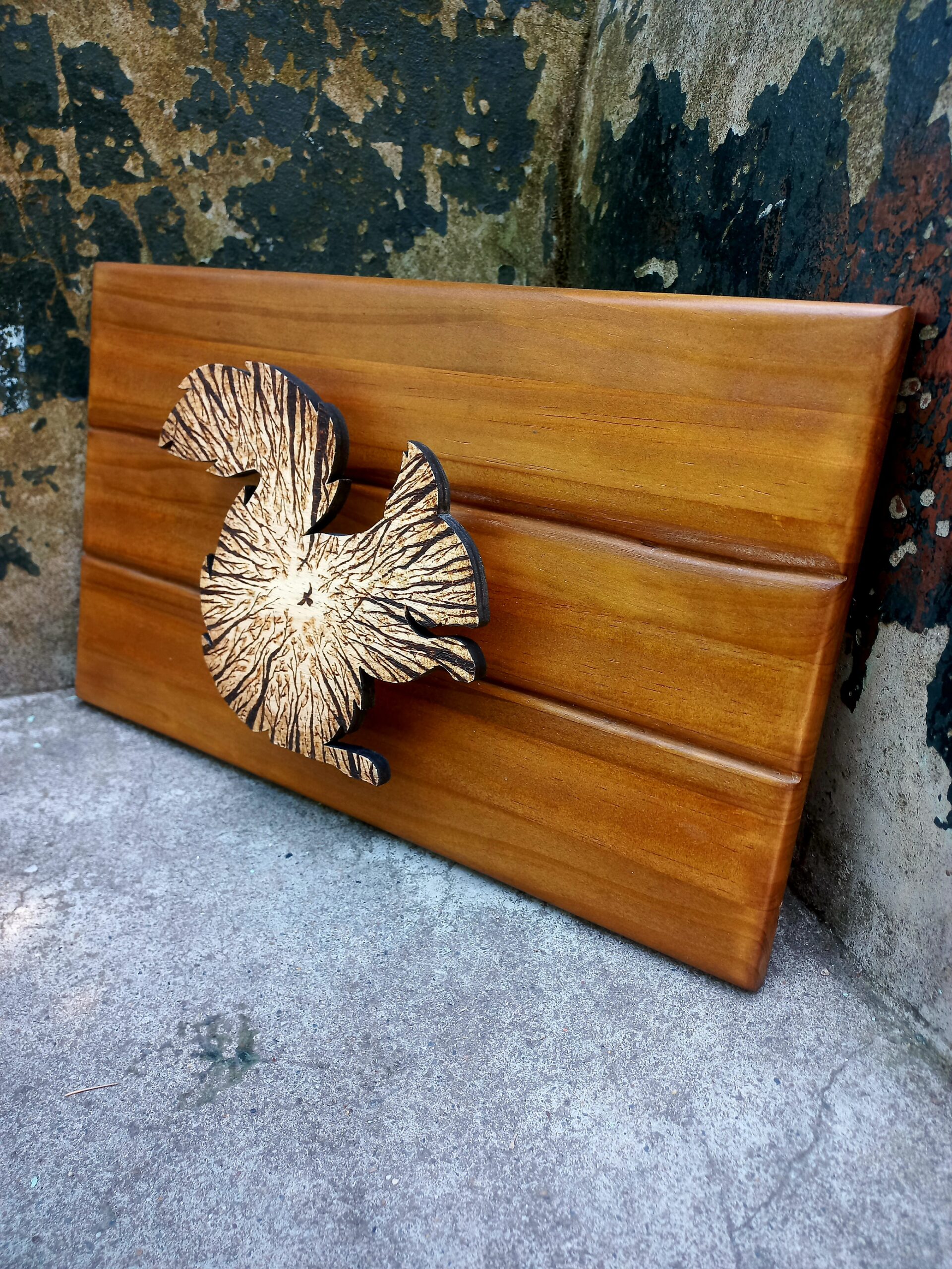 Cadro de madeira composto por unha peza coa silueta dun esquío, cuxo interior mostra un pirogravado que representa a visión do animal desde o chan mirando cara ás copas das árbores.