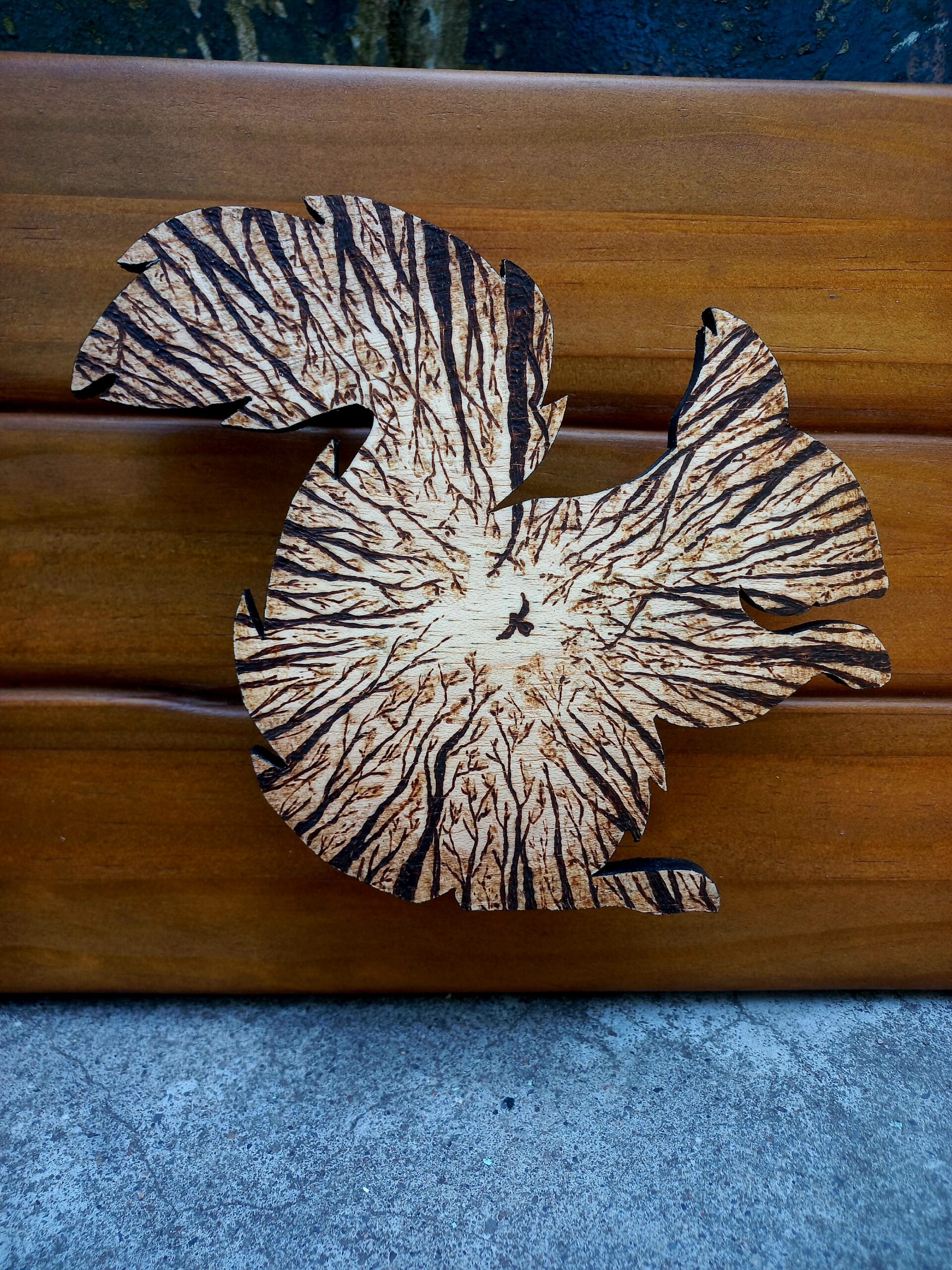 Cadro de madeira composto por unha peza coa silueta dun esquío, cuxo interior mostra un pirogravado que representa a visión do animal desde o chan mirando cara ás copas das árbores.