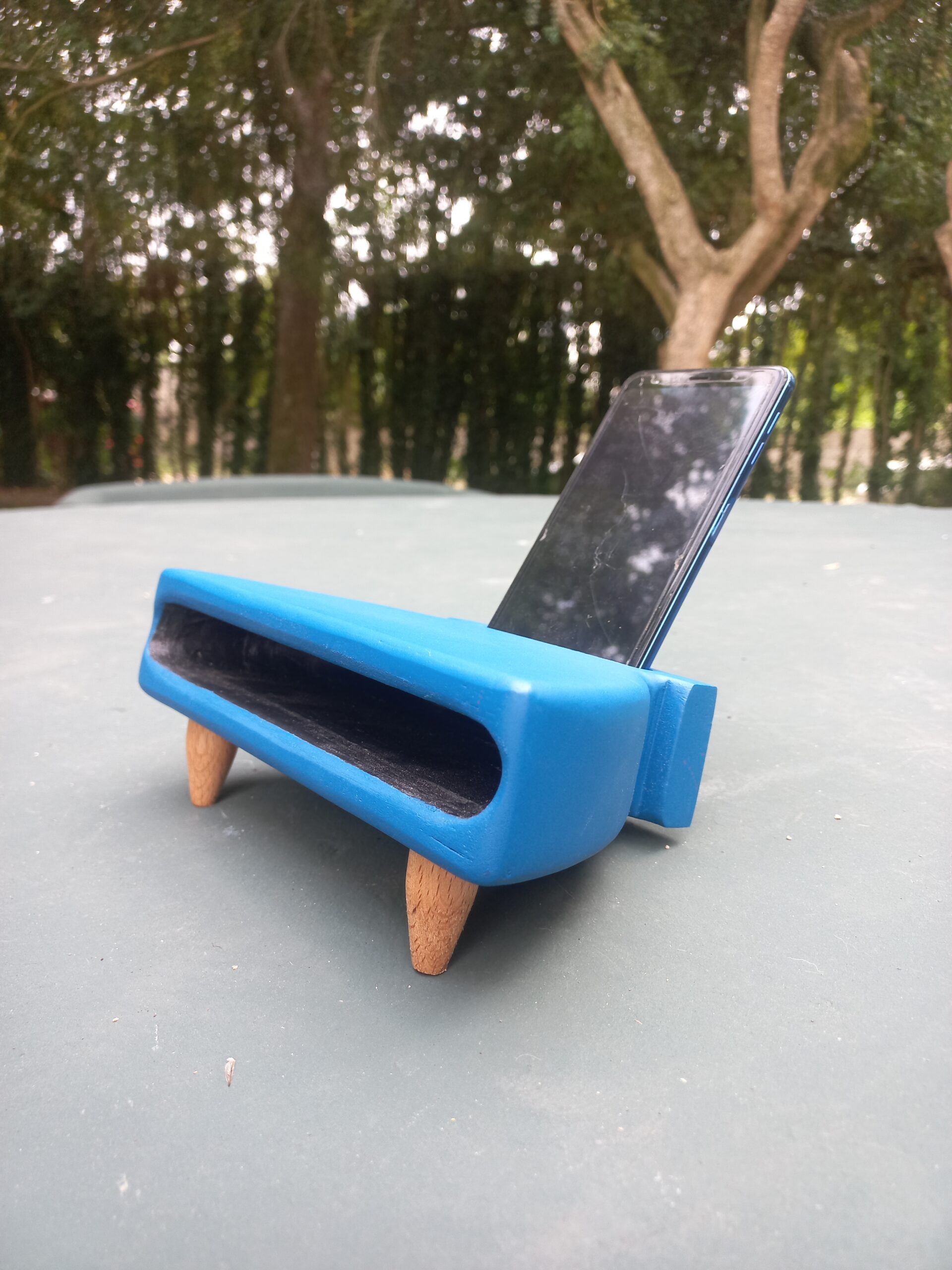 Altofalante pasivo artesanal feito en madeira e resina azul, con cavidade frontal para amplificar o son dun móbil apoiado na parte traseira.