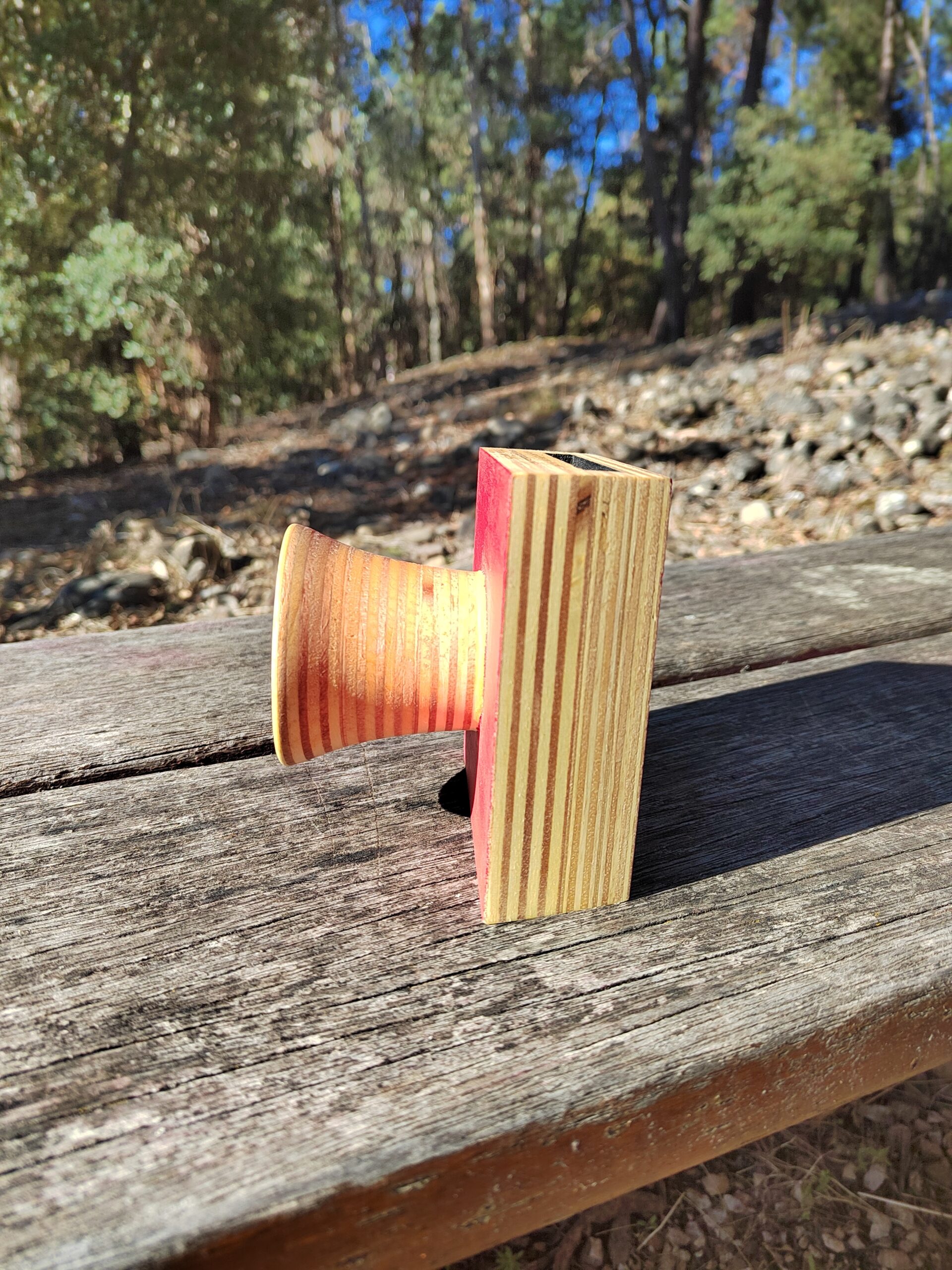 Amplificador de son pasivo artesanal en madeira con panel vermello e bocina frontal torneada, cun smartphone colocado na ranura superior.