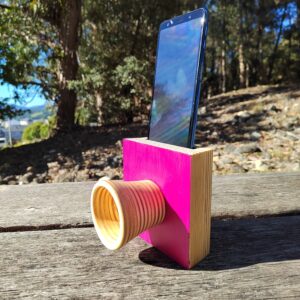 Amplificador de son pasivo artesanal en madeira con acabado fucsia e bocina frontal, cun smartphone colocado na ranura superior.