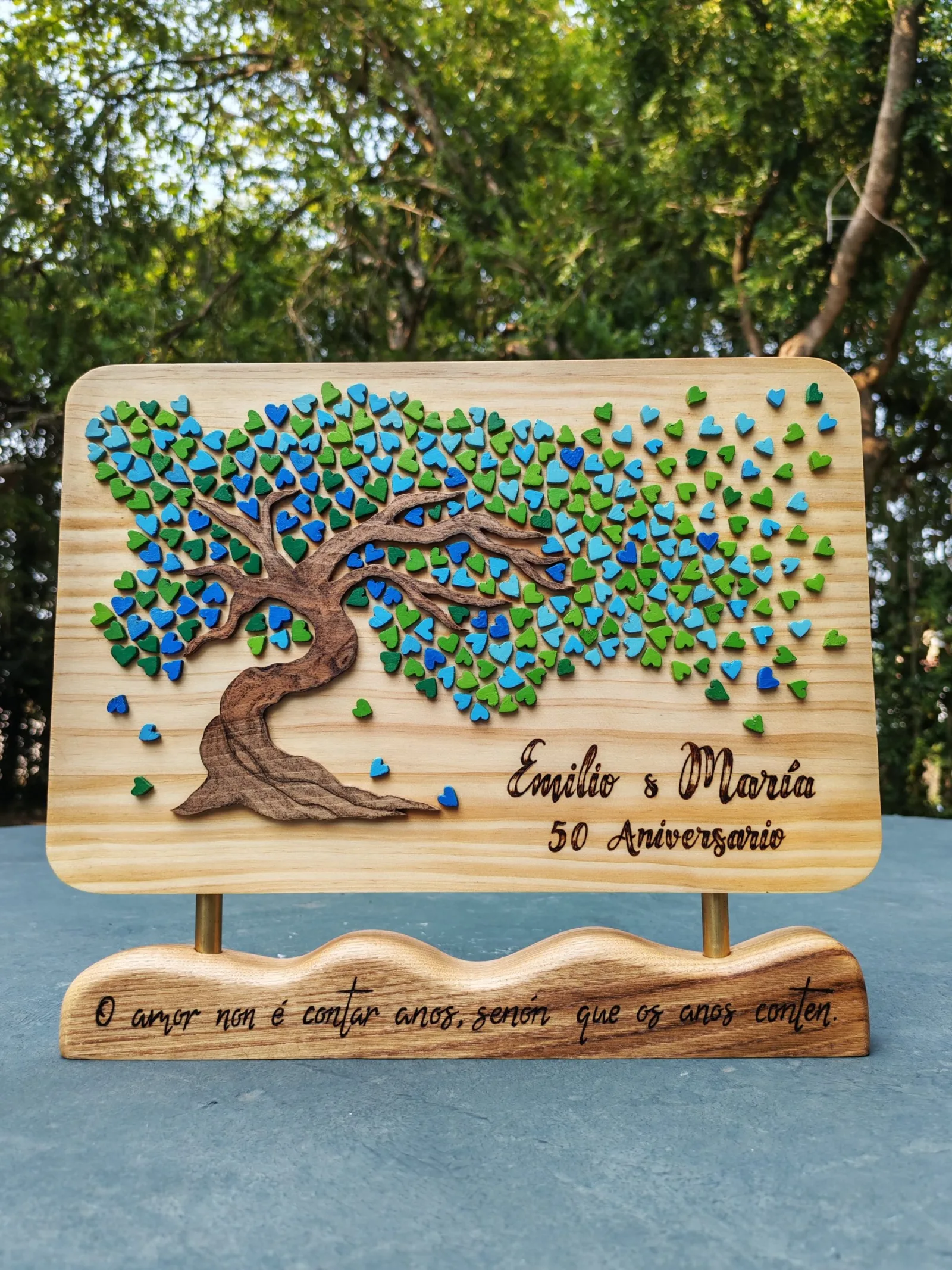 Árbore da vida de madeira en relevo con corazóns azuis e verdes, co nome dun casal e a frase O amor non é contar anos, senón que os anos conten pirogravada na base