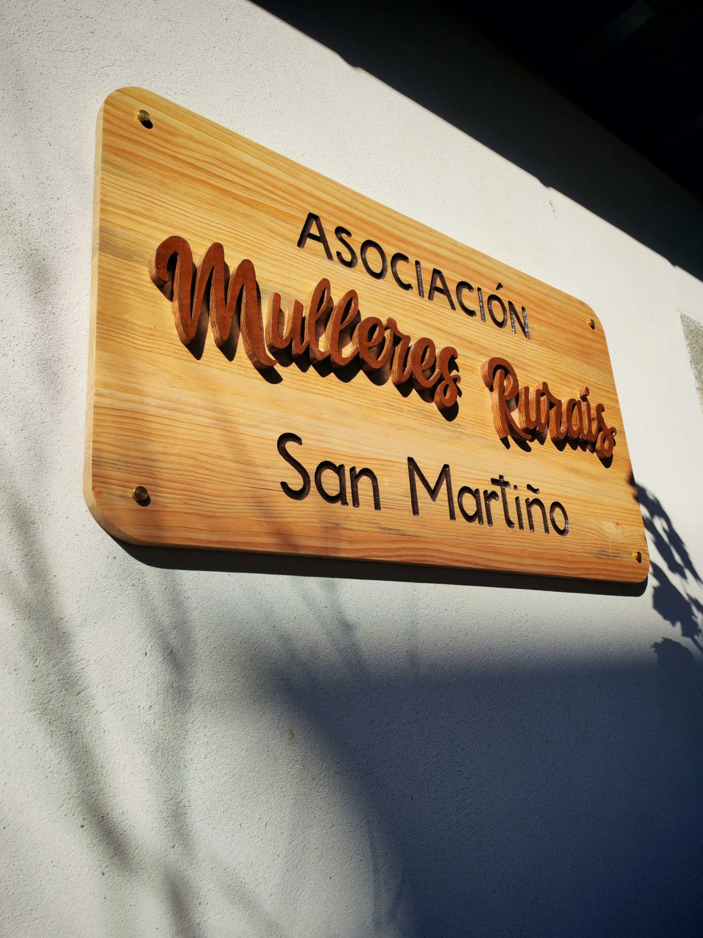 Cartel de madeira con letras en relevo «Asociación Mulleres Rurais San Martiño», colocado na fachada