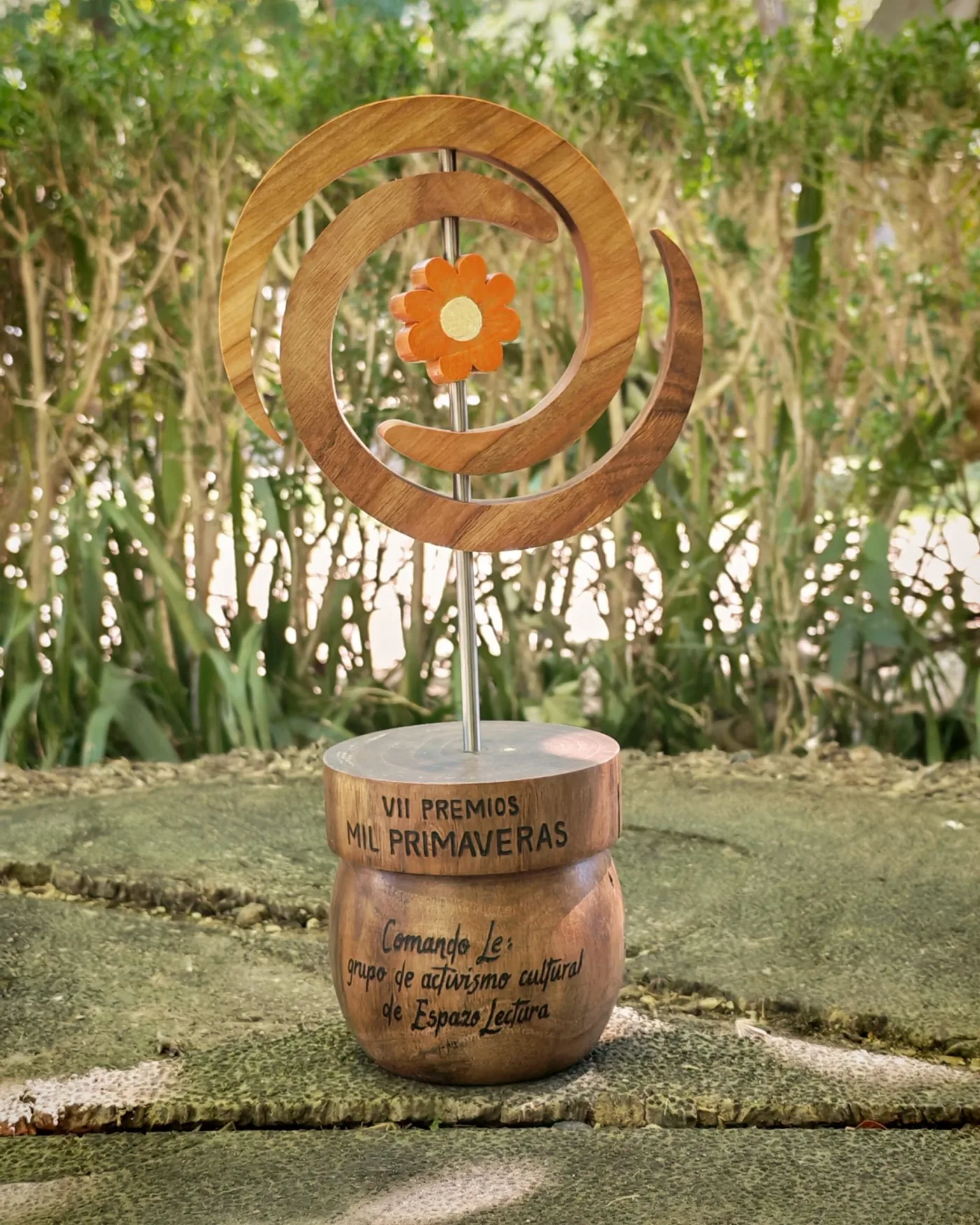 Premio Mil Primaveiras: espiral de madeira cunha flor laranxa sobre unha peana de madeira pirogravada