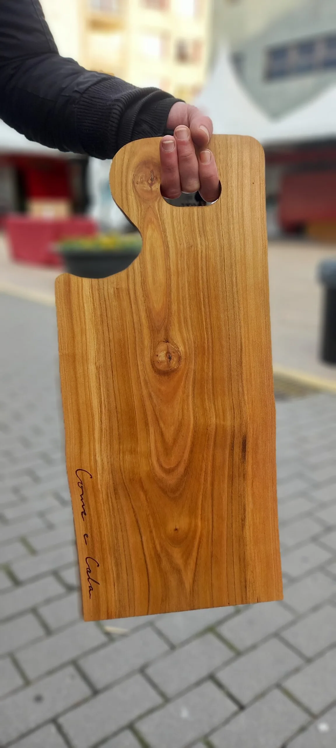 Táboa de corte de madeira de cerdeira con asa e unha dedicatoria, sostida coa man